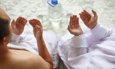 Close up shot of muslim couple wearing white ihram clothes, praying before drinking zam zam water.